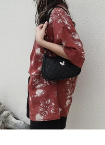 Detail of black quilted crescent bag with butterfly hardware on floral dress model