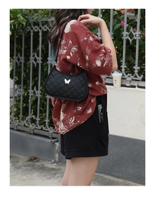 Close-up of black quilted shoulder bag with silver butterfly buckle on outdoor model