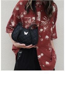 Detail of black quilted moon bag with white butterfly charm on woman's shoulder
