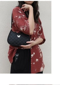 Close-up of black quilted shoulder bag featuring white butterfly ornament and zipper detail
