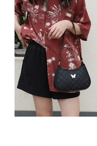 Detail of black quilted shoulder bag with a silver butterfly metal emblem on the surface
