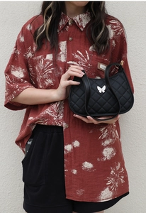 Close-up of black quilted shoulder bag featuring a white butterfly accessory and classic texture