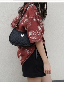 Detail of a black quilted shoulder bag featuring a silver butterfly buckle decoration
