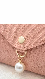 Detail display of pink woven phone bag with gold clasp and elegant pearl pendant