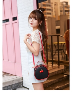 Close-up of a round lychee-textured crossbody bag with cherry decor on a female model