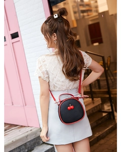 Outdoor shot of a black litchi pattern round crossbody bag with red cherry decoration
