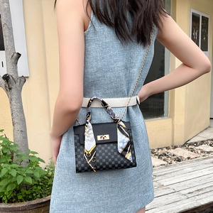 Black polka dot crossbody bag with gold chain strap and silk scarf on a model