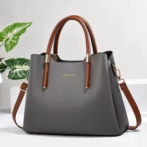 Graue Handtasche mit Litschi-Maserung, braunen Griffen und goldenen Details auf weiß