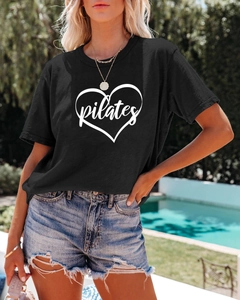 Detail of black cotton T-shirt featuring a white Pilates heart print in a poolside setting