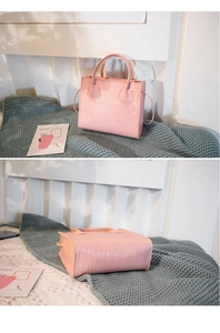 Detail view of pink crocodile embossed handbag with dual handles and long shoulder strap