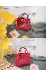 Close-up detail of red crocodile pattern handbag with dual handles and long shoulder strap