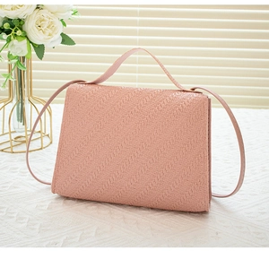 Pink woven handbag with matching shoulder strap on an elegant white table background