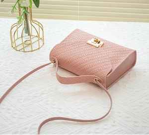 Detail of pink woven texture crossbody bag with gold twist lock on a vintage table