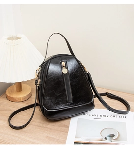 Close-up of a black glossy mini backpack with gold hardware on a wooden table