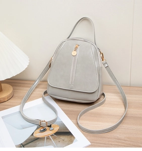 Detail view of a gray PU leather multi-layer shoulder bag with golden zippers on wood