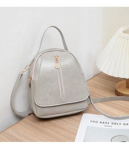 Detailed view of light grey PU leather backpack featuring polished texture and zip accents