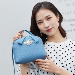 Borsa azzurra con motivo litchi e fibbia a ape dorata mostrata dalla modella