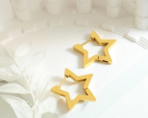 Macro detail of geometric gold star earrings on an elegant white textured background