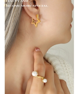 Close-up of minimalist gold star stud earrings and double pearl open ring on model