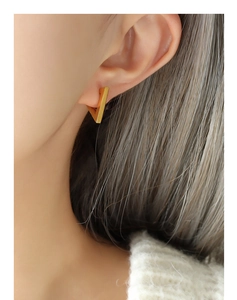 Macro view of minimalist matte gold triangular geometric stud earrings worn on ear