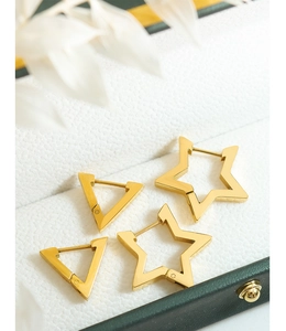 Detailed close-up of gold geometric star and triangle earrings on a white jewelry pad