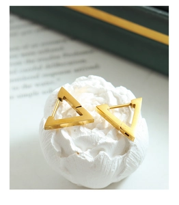 Detailed view of gold triangle hoop earrings resting on a white decorative floral prop