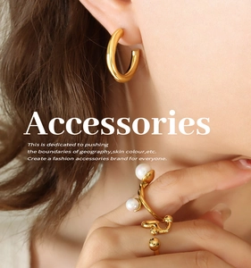 Nahaufnahme eines klobigen goldenen C-Ohrrings und eines Perlenrings am Model