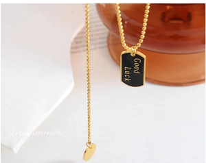 Makrodetail der goldenen Kugelkette mit schwarzem Good Luck Rechteckanhänger