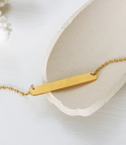 Gros plan du pendentif barre dorée avec gravure Good Luck sur chaîne en acier titane