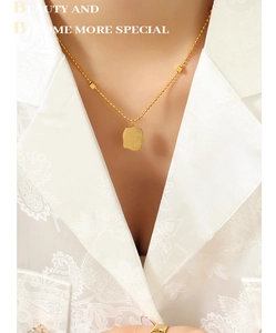 Close-up of gold titanium necklace with irregular square pendant and Good Luck engraving