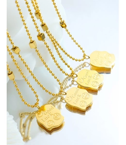 Macro detail of gold-plated square pendants featuring smile emoji and Good Luck engraving