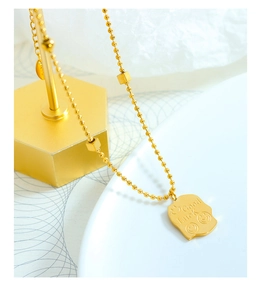 Detail of golden bead chain necklace with engraved Good Luck square tag and smiley face