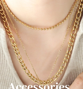 Close-up of triple-layered gold chain necklaces featuring a chunky curb link on knitwear
