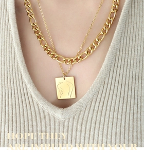 Macro detail of gold layered necklaces with line art woman figure square pendant