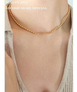 Close-up of elegant gold beaded necklace worn on a beige ribbed knit sweater