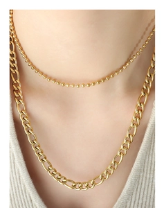 Close-up of layered gold ball and Figaro chain necklace on a model wearing knitwear
