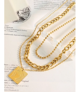 Close-up of triple-layered gold necklaces featuring an abstract face relief square pendant