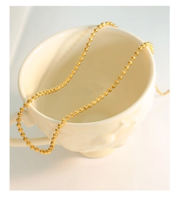 Detailed macro view of a 18K gold bead chain necklace hanging on a ceramic cup edge