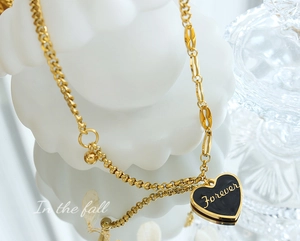 Macro view of golden heart necklace with black enamel and Forever engraving detail