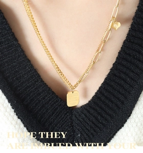 Close-up of golden double-layered chain necklace featuring heart and letter plaque charms