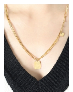 Detailed view of layered gold chain necklace with engraved rectangle and heart pendants