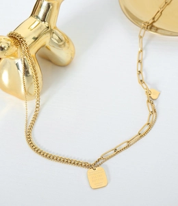 Detail of gold double chain necklace with engraved rectangular tag and small heart pendant