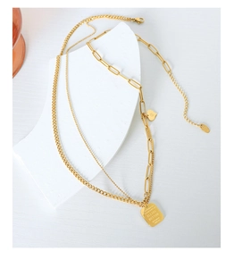Detail of gold double chain necklace with engraved rectangular pendant and heart charm