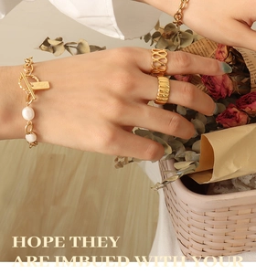 Detail of OT buckle gold bracelet with pearls and textured rings on a vintage backdrop