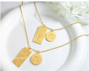 Gros plan du collier double pendentif doré avec plaques gravées sur un plateau blanc