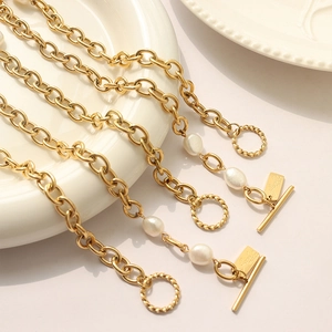 Golden chunky chain bracelet with freshwater pearls and square tag on ceramic plate