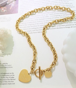 Détail d'un collier à grosse chaîne dorée avec pendentif cœur et fermoir à bascule sur revue