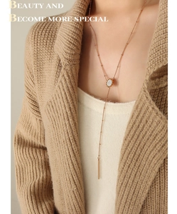 Dettaglio della collana lunga in oro rosa con pendente in cristallo e nappa su maglione