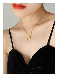 Primo piano di una collana in titanio dorato con perla barocca e ciondolo irregolare