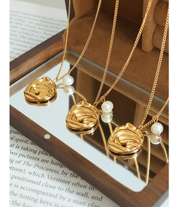 Dettaglio ravvicinato del ciondolo a rosa dorata con perla d'acqua dolce e metallo satinato